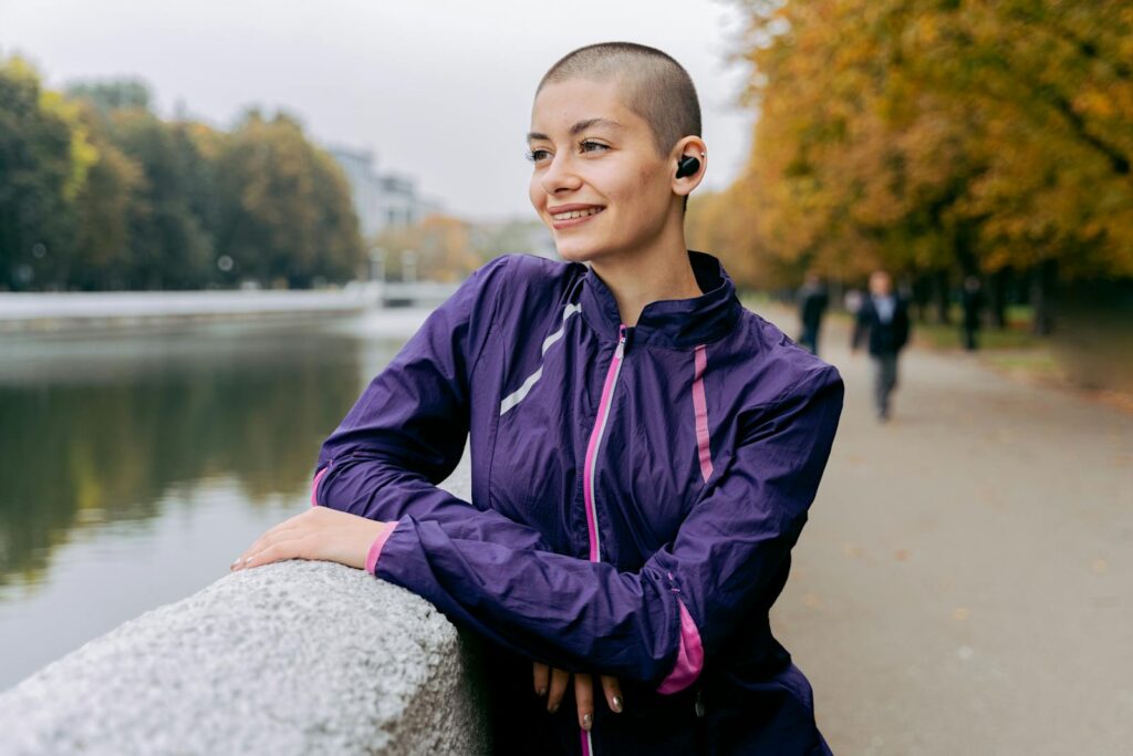 Bald woman in purple active wear smiling by a riverside in autumn.