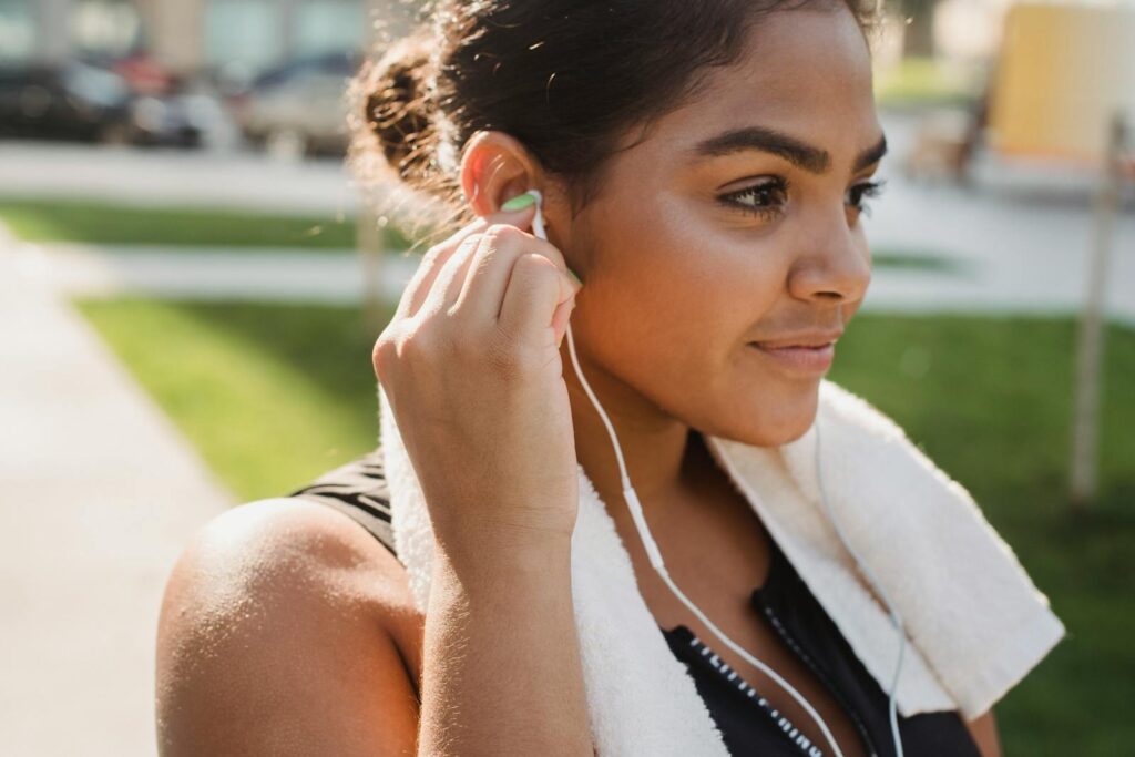 Young woman smiling and wearing earphones, preparing for an outdoor workout on a sunny day.