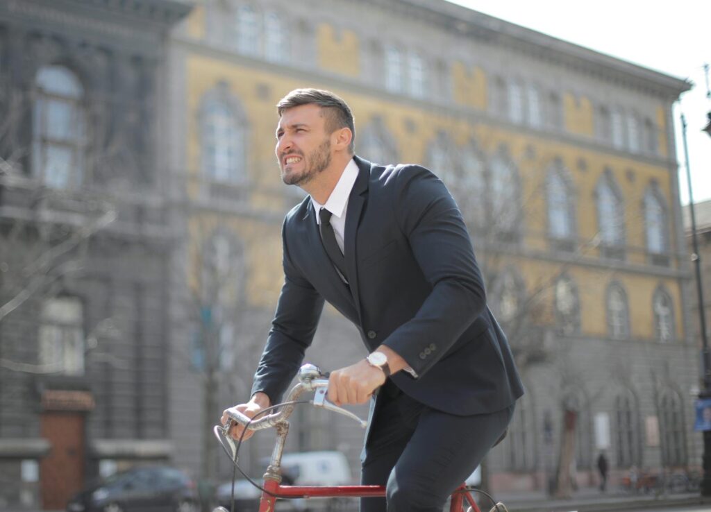 Man in formal attire cycling through a city street during the day.