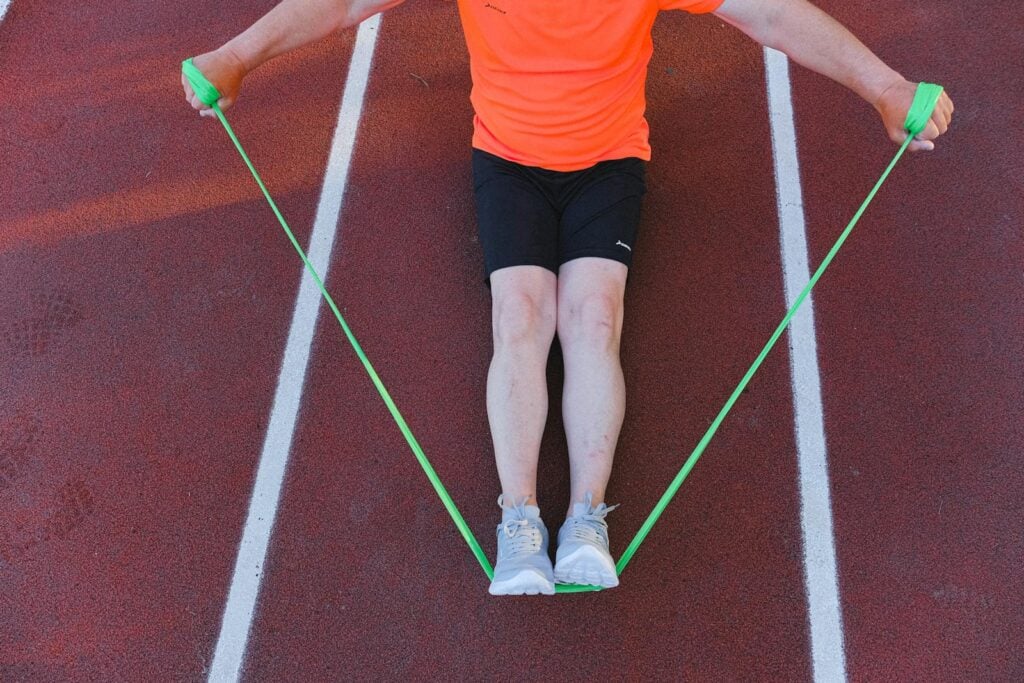 An adult male athlete working out with a green resistance band on a running track. Perfect for fitness and wellness themes.