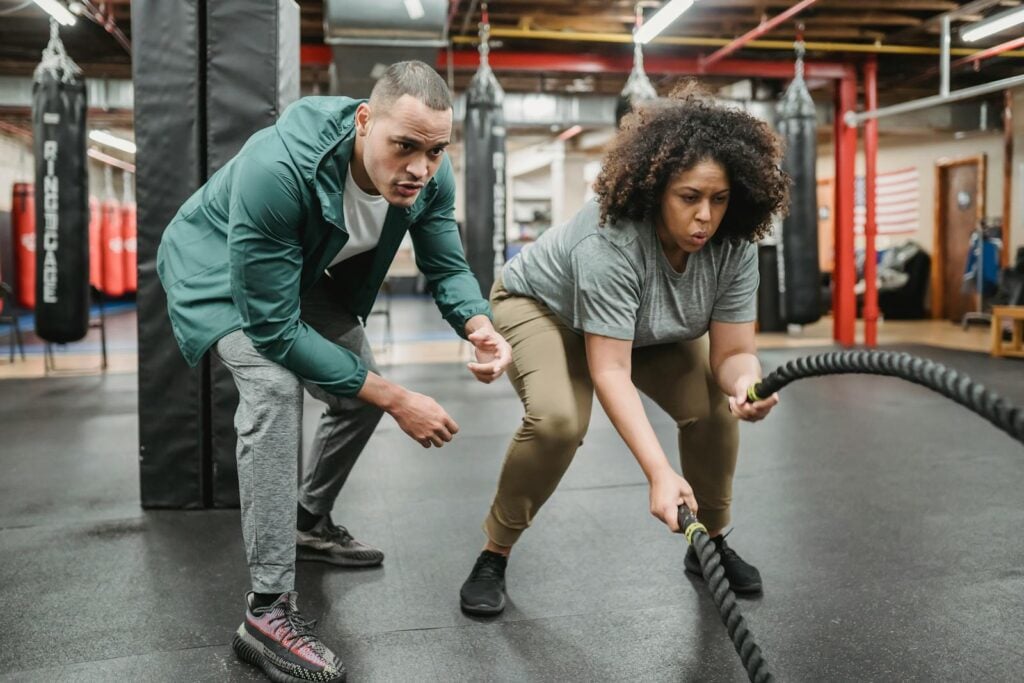 A dedicated woman focuses on battle rope training, guided by her fitness coach.