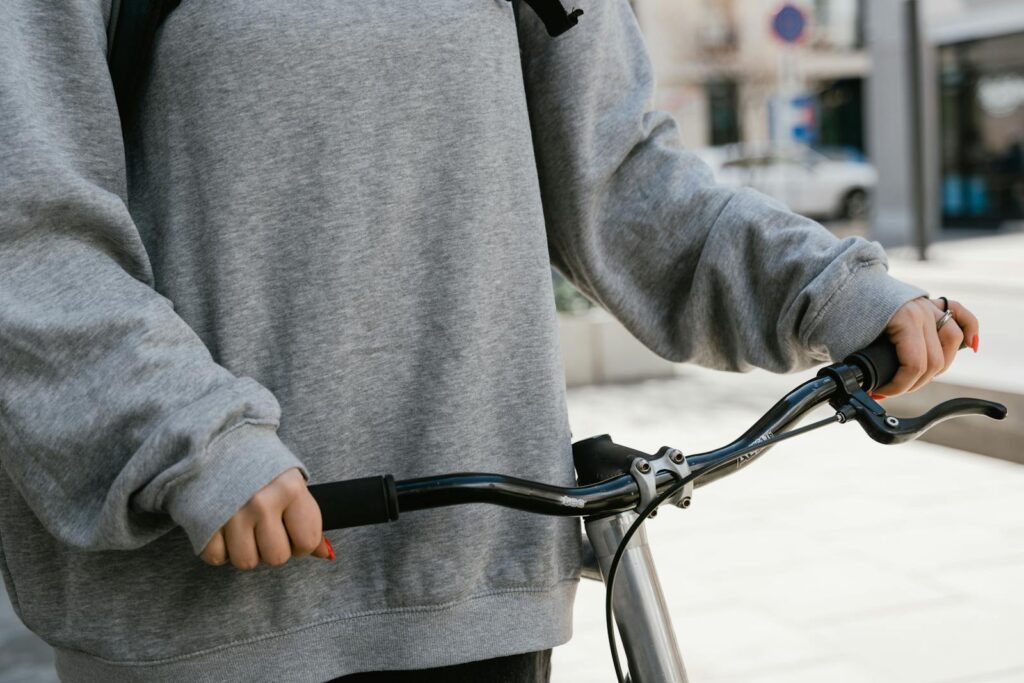 A person in casual attire gripping bicycle handlebars in an outdoor urban setting.